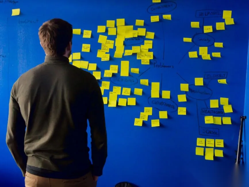 Best Competitor Analysis Tools for AI Search Optimization 2025 Person studying a wall of yellow sticky notes, mapping competitors for AI search optimization