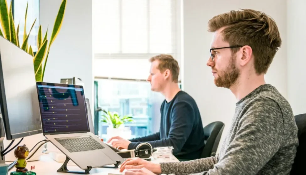 Two colleagues working at laptops in a bright office, the everyday HR admin an AI tool for HR teams takes on