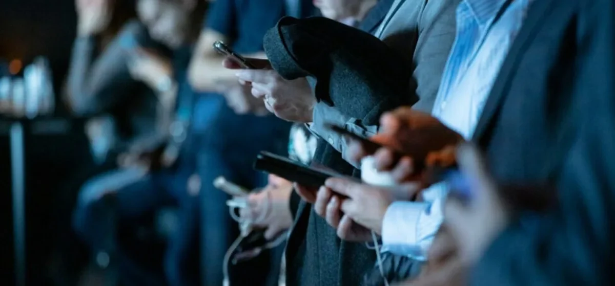 People in a crowd checking their phones, where Google AI Overviews now answer many searches