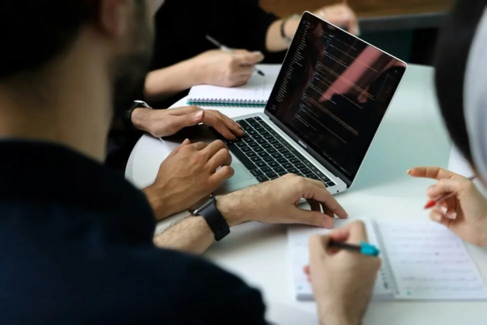 A group of people sitting around a laptop in a meeting, the stack-buying conversation the best AI tools for SEO marketing 2026 are chosen in