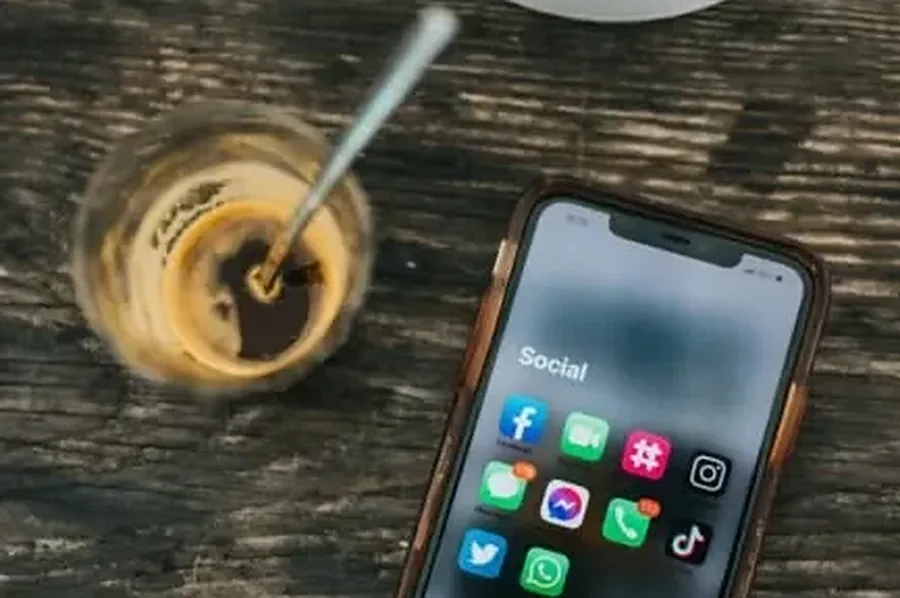 Phone with social media apps beside a coffee, where consumer goods shoppers ask AI assistants for recommendations