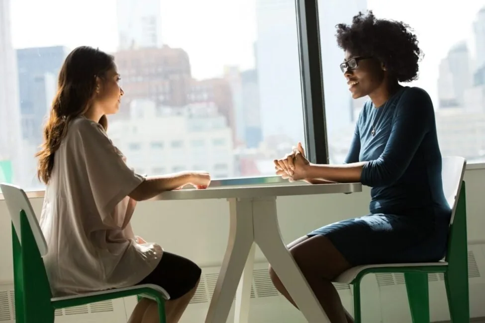 Two women talking across a table in an interview, the conversation free AI HR tools for Mac 2026 transcribe and summarise