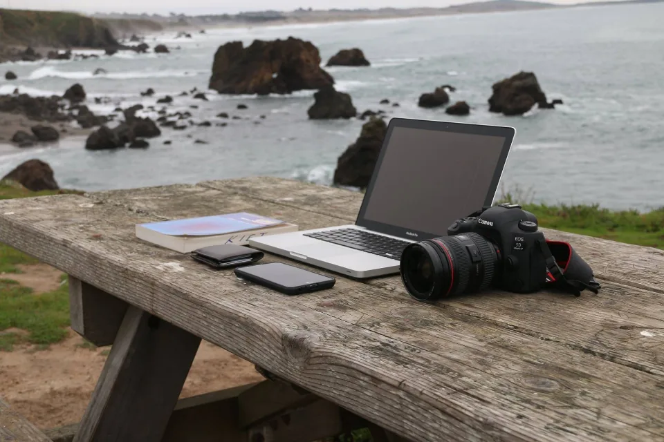 Laptop and camera on seaside table Laptop and camera on a wooden table by the sea, a portable machine for testing small local models